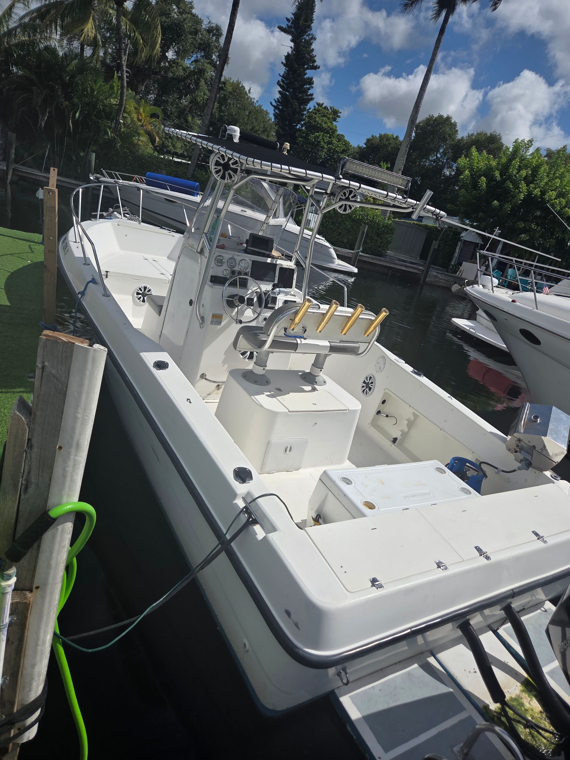 White fishing boat docked on a canal, with fishing rods and equipment visible, sunny day.