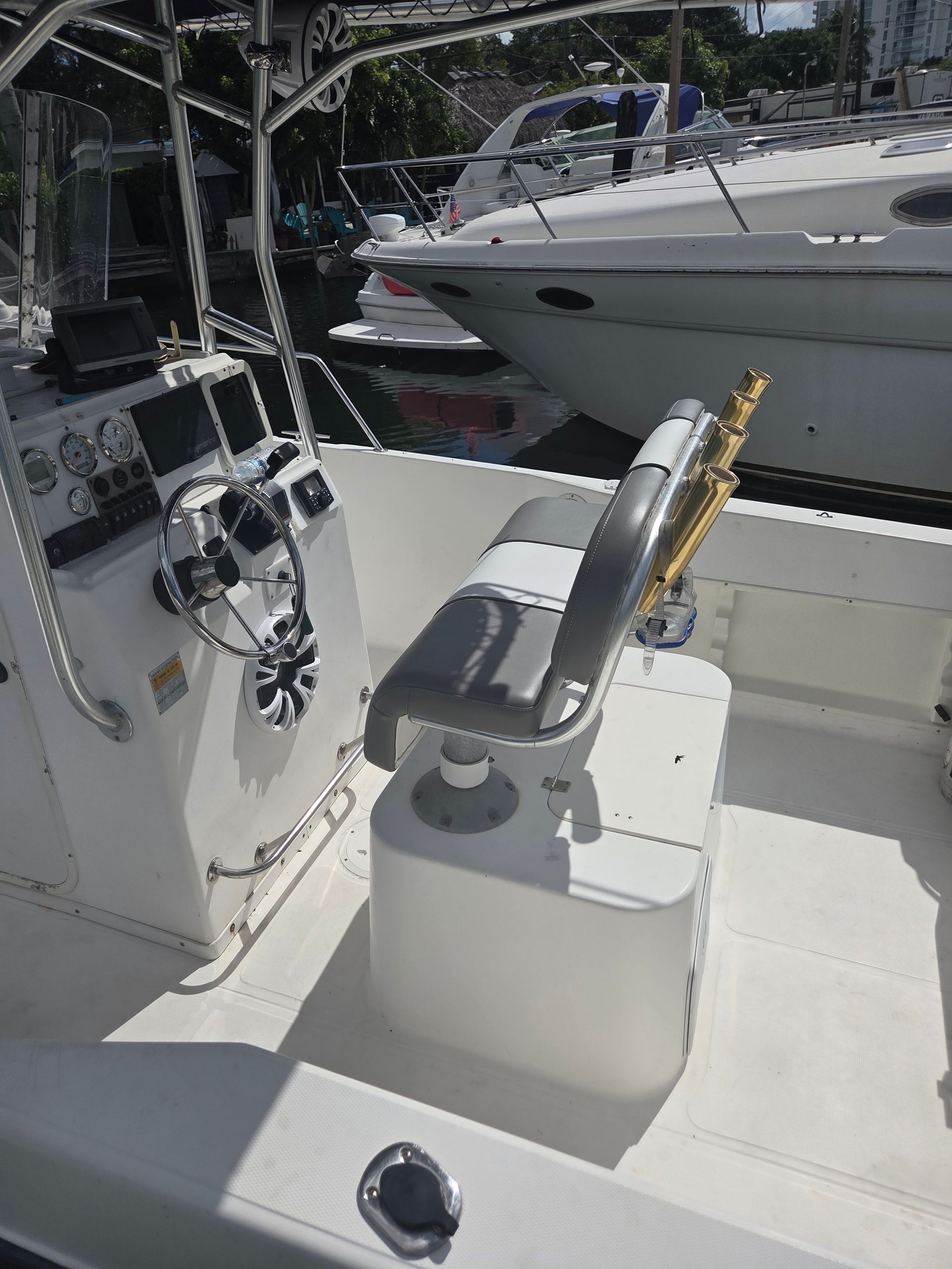 Boat cockpit with white deck and gray helm seat; other boats in background.