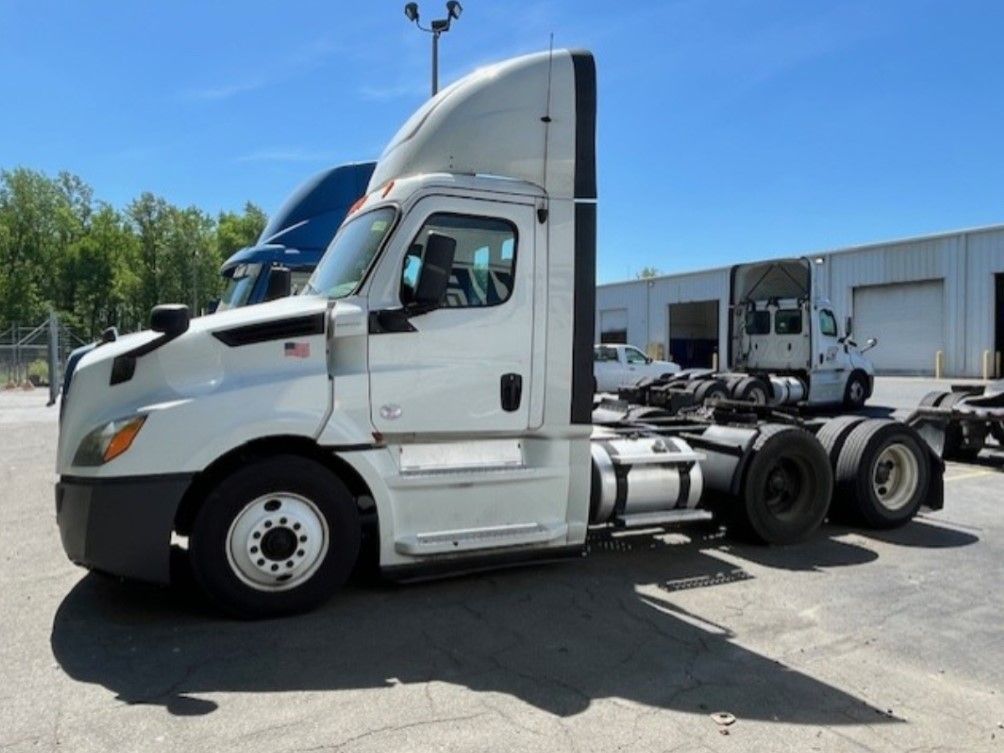 White semi-truck parked outside on a sunny day, with other trucks and buildings in the background.