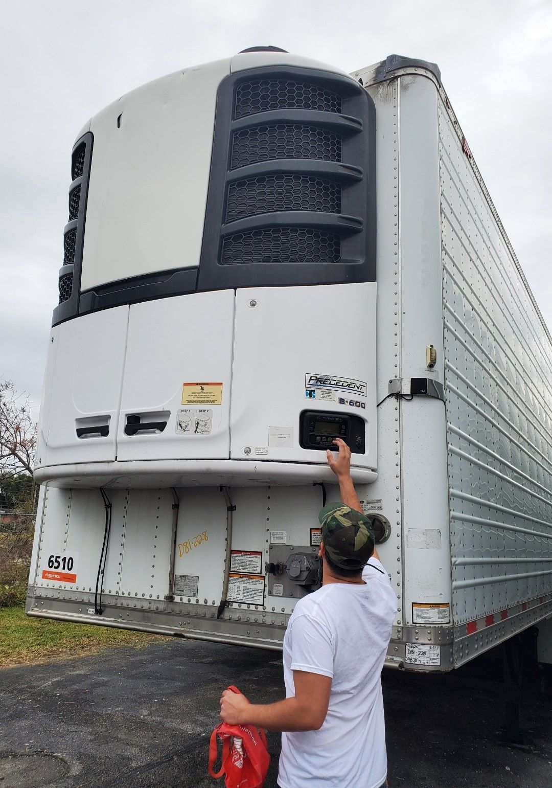 Man near a white refrigerated trailer, possibly checking the refrigeration unit.