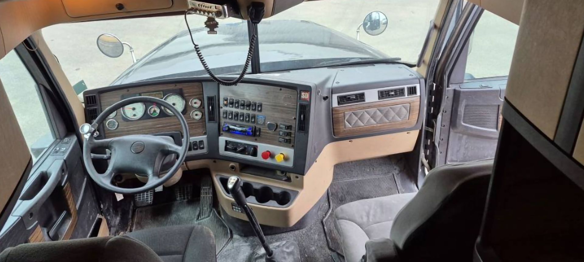 Interior view of a truck cab with dashboard, steering wheel, seats, and open doors.