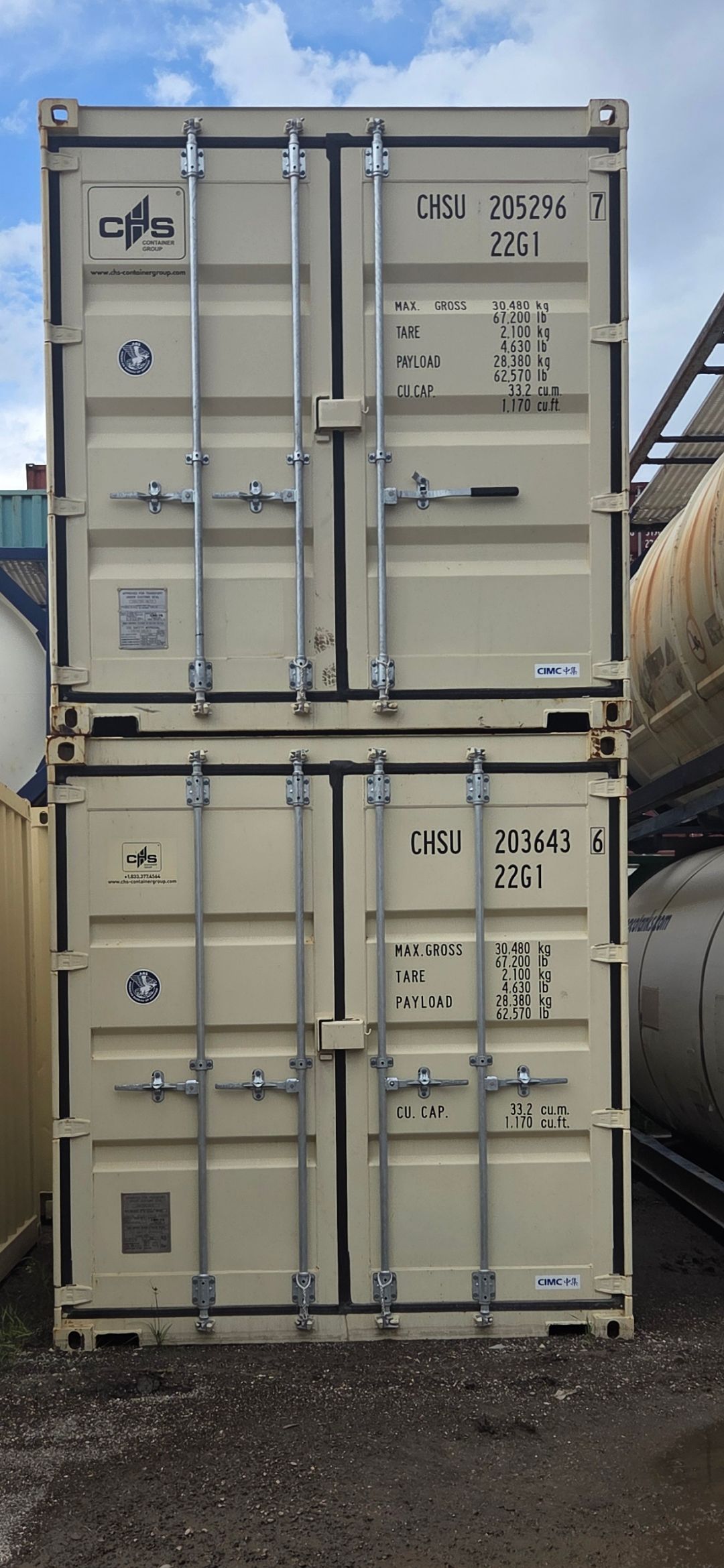 Two beige shipping containers stacked on top of each other under a partly cloudy sky.