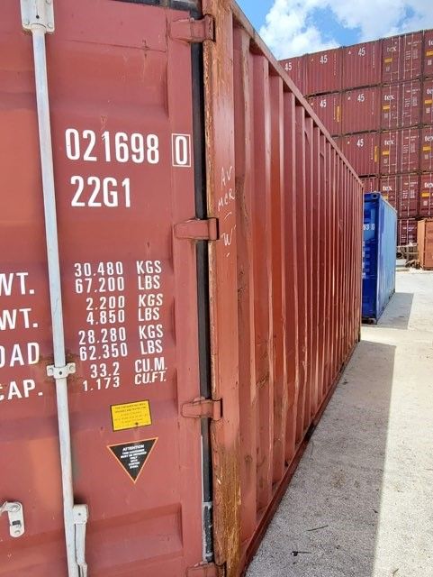 Red shipping container with numbers and specs labeled on its side, outdoors.