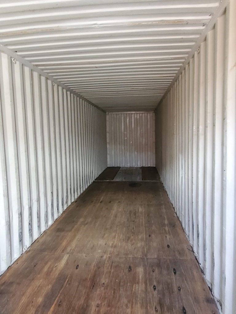 Empty shipping container interior with white ribbed walls and wooden floor.