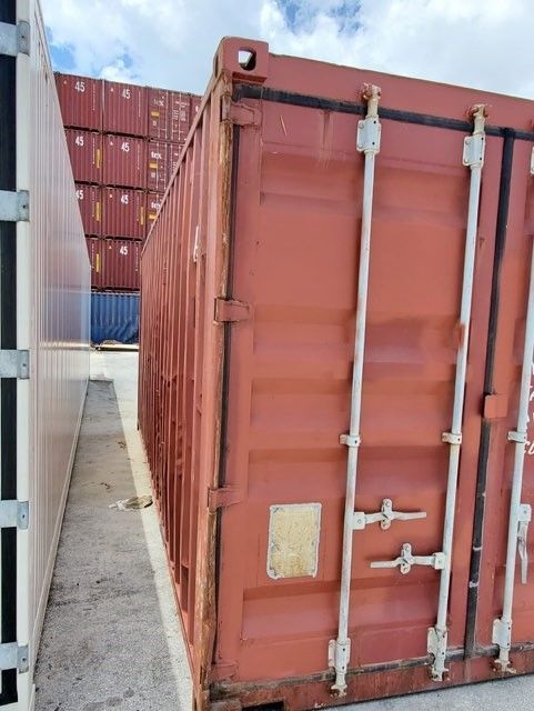 Red shipping container in an industrial lot, stacked containers in the background.