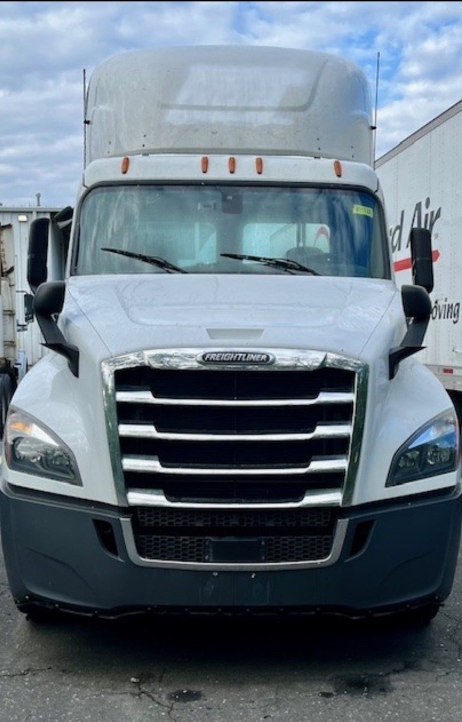 White Freightliner semi-truck with black grill, side mirrors, and headlights. Gray bumper.