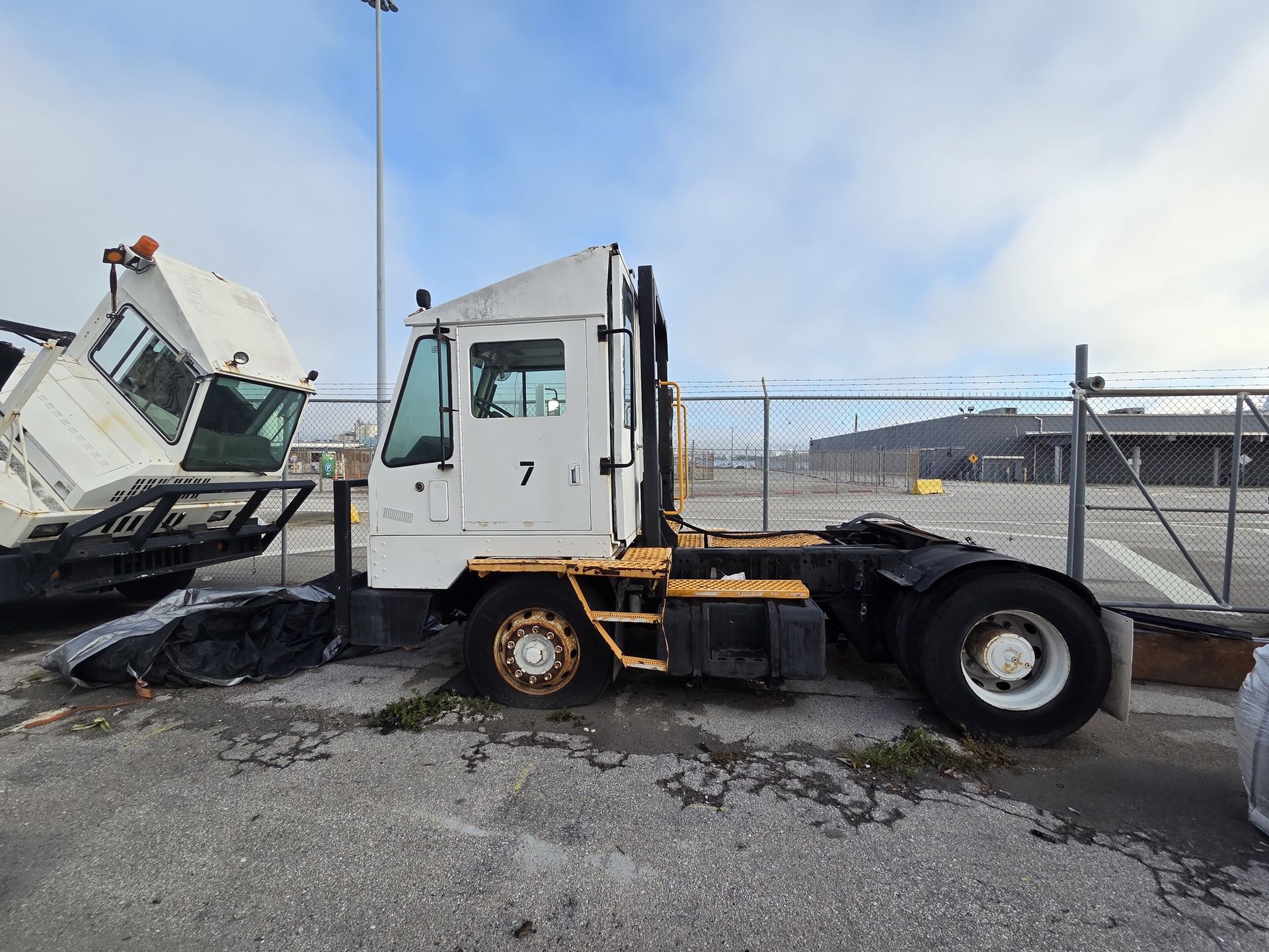 White and yellow terminal tractor in an industrial yard.