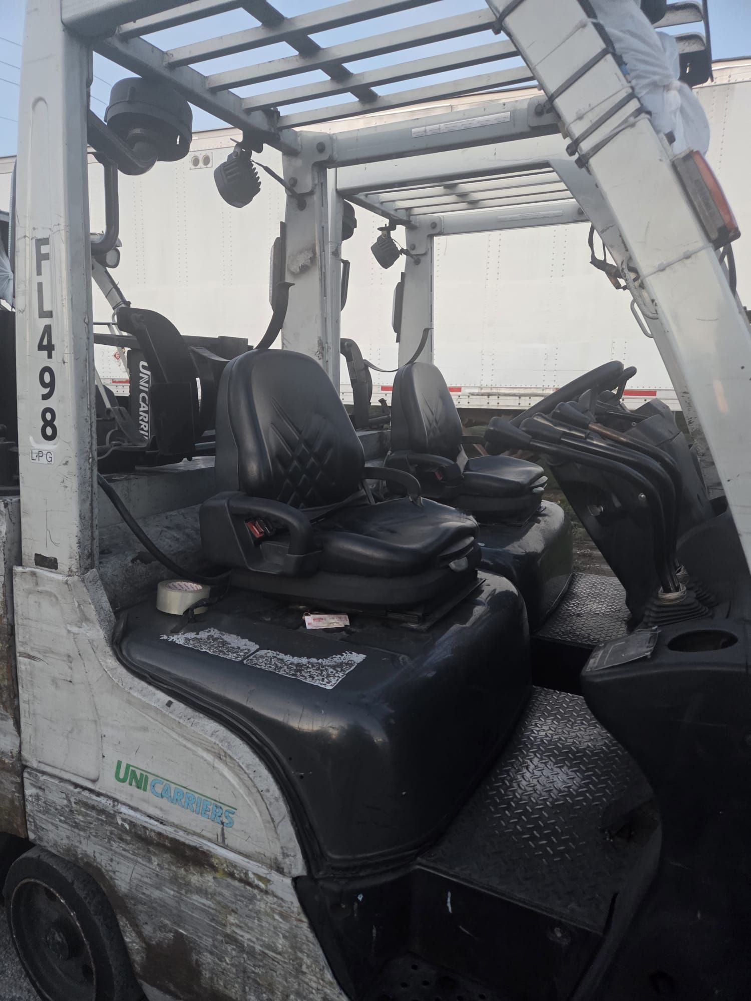 White forklift with black seat, controls, and overhead guard; parked outside, near other forklifts.