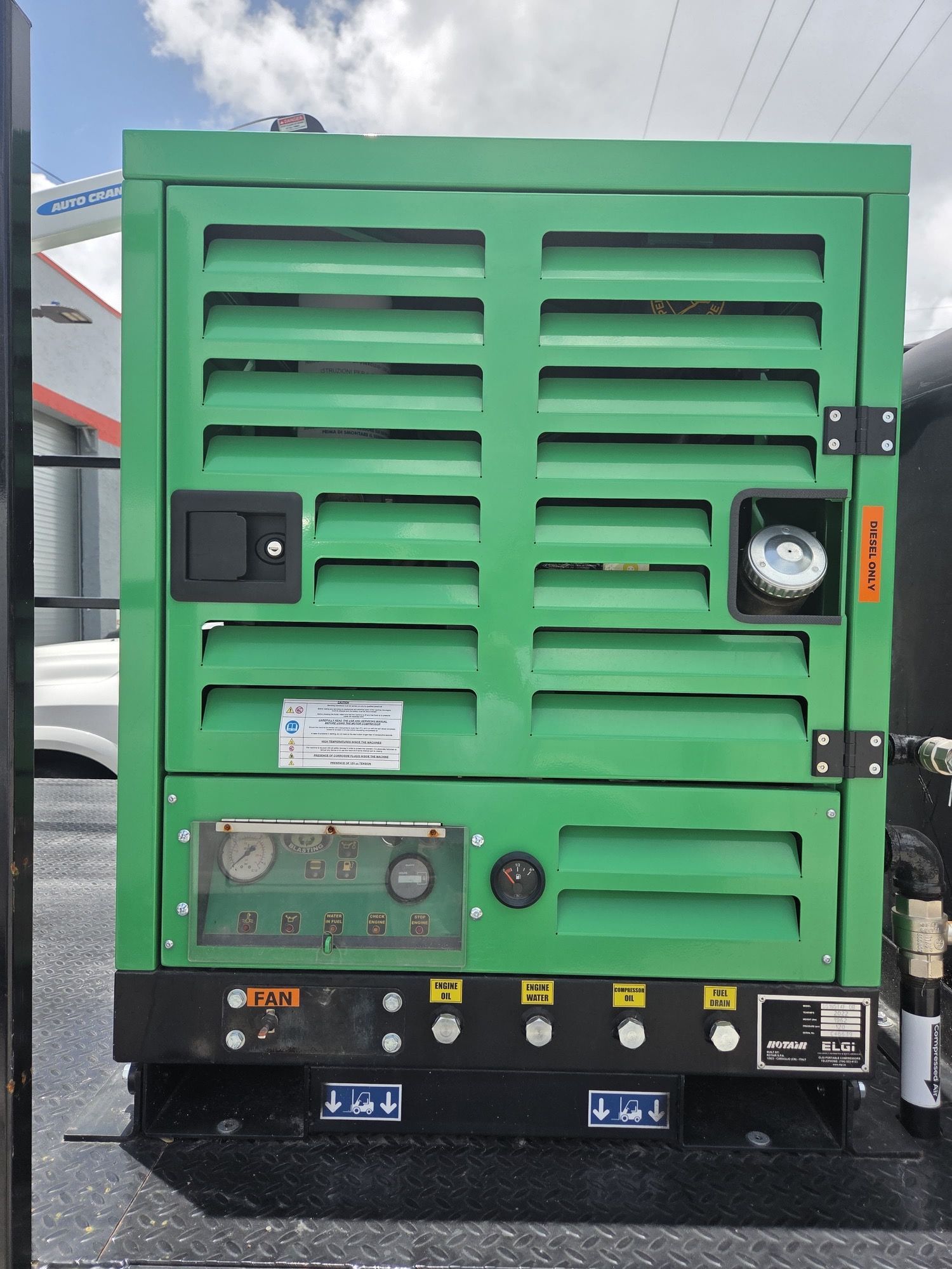 Green generator with horizontal vents, gauges, and control panel on a truck bed.