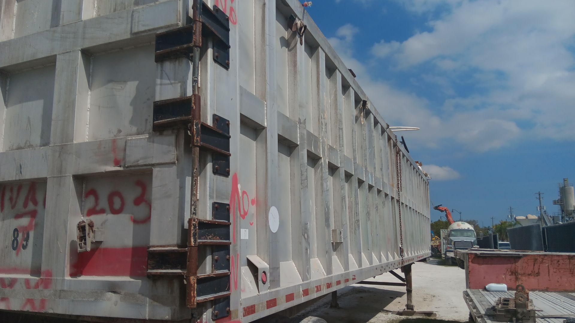 Large silver dump trailer with visible side details parked outdoors against a blue sky.