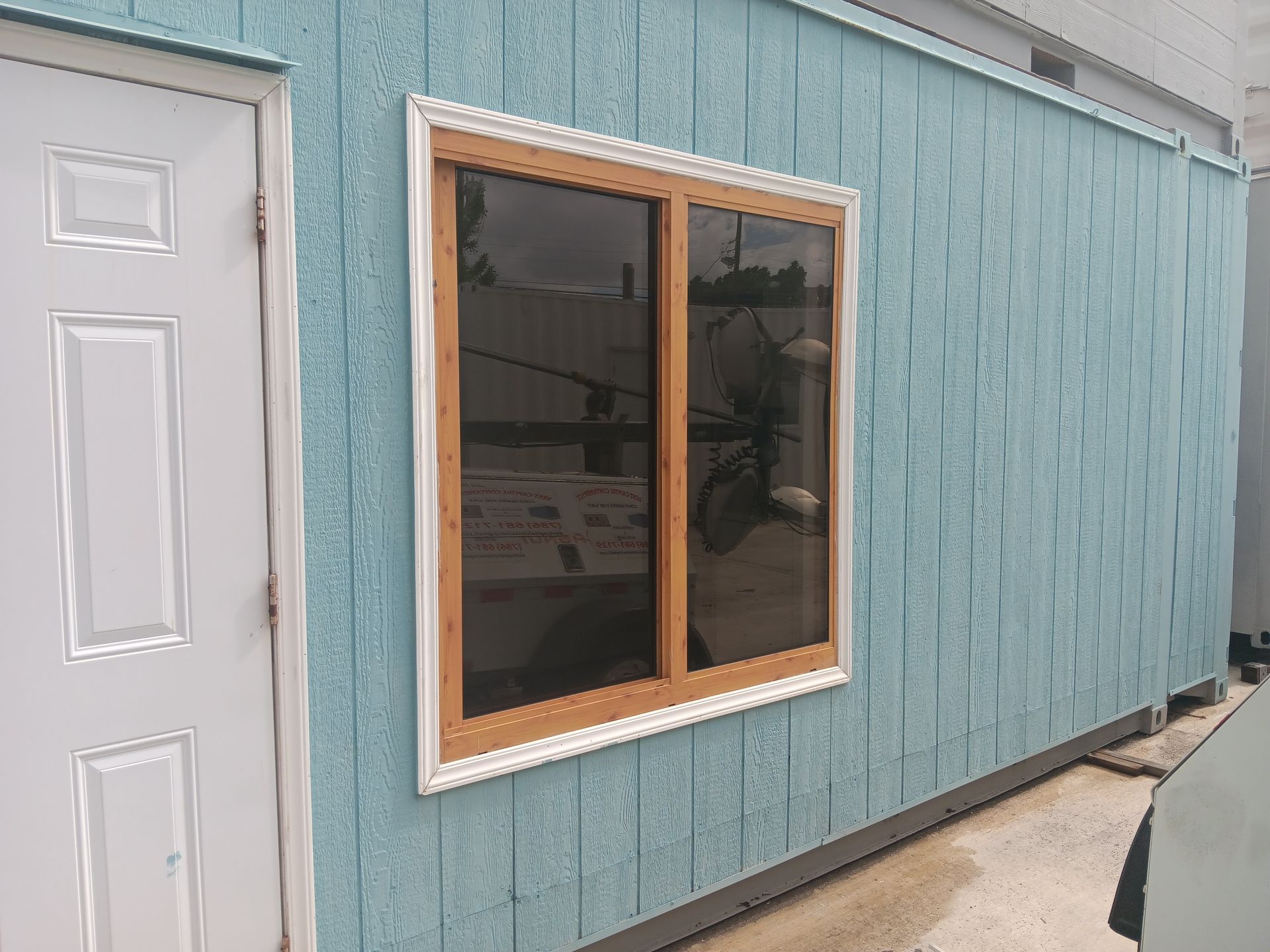 Blue building exterior with a window and white door. The window has brown framing and tinted glass.