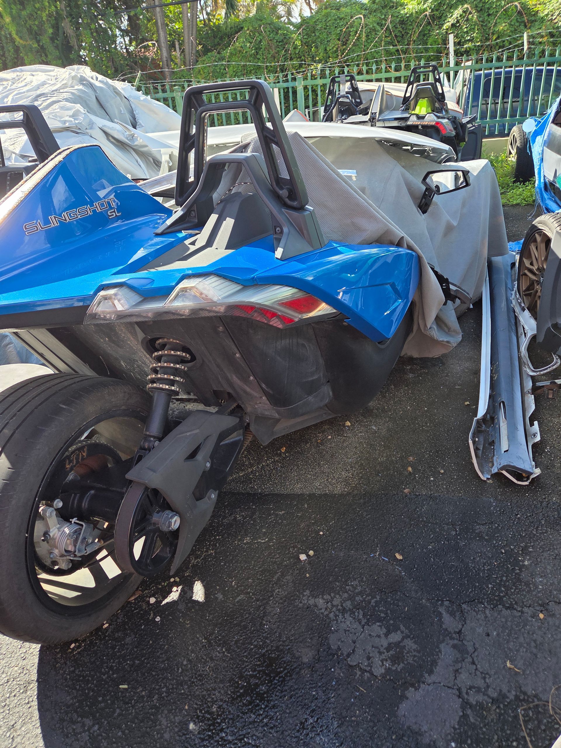 Blue Polaris Slingshot with rear damage, parked outdoors.
