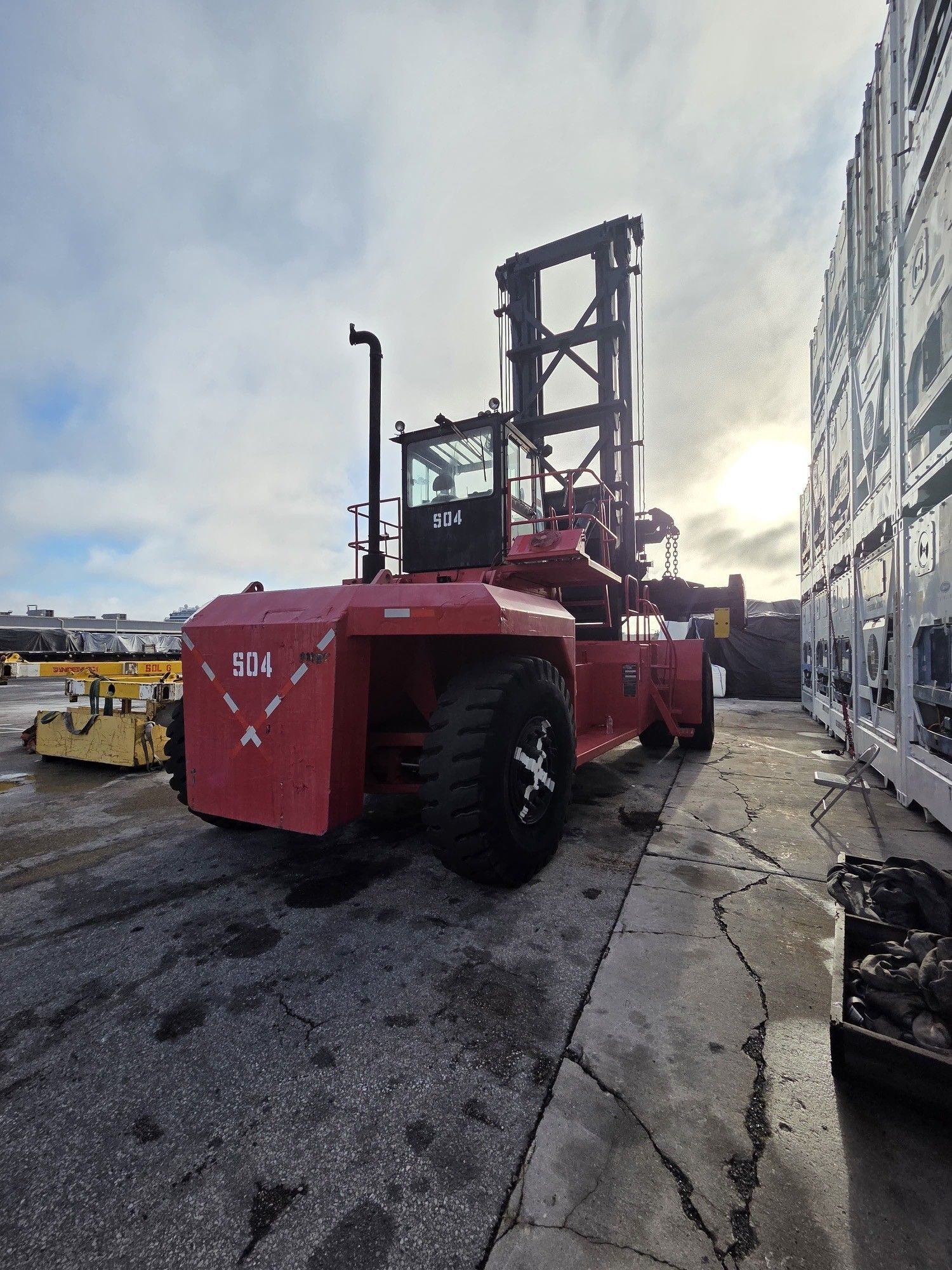 Red container forklift near stacked containers on a cloudy day.