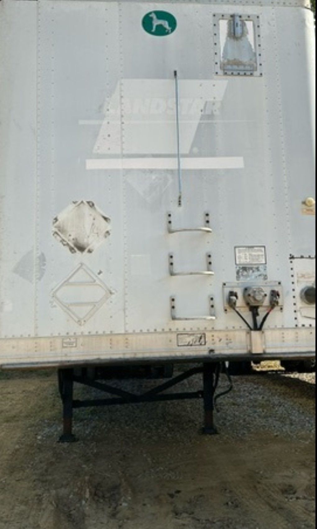 White semi-trailer side with a green dog logo, a ladder, and a black undercarriage.