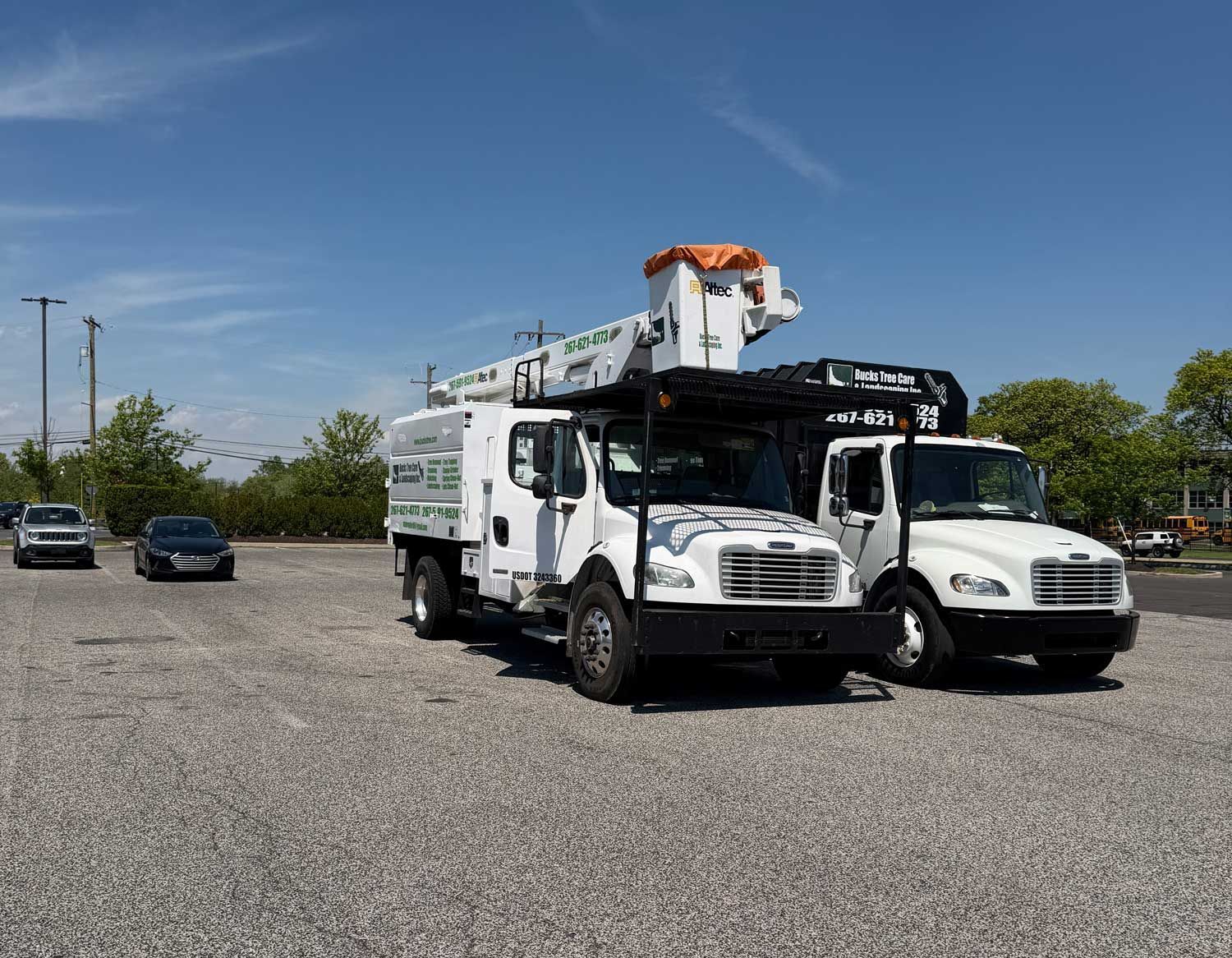 Two white tow trucks parked on a gravel lot under a clear blue sky