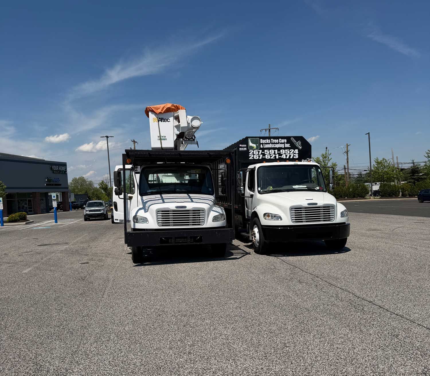 Two white utility trucks parked side by side in a gravel lot under a blue sky