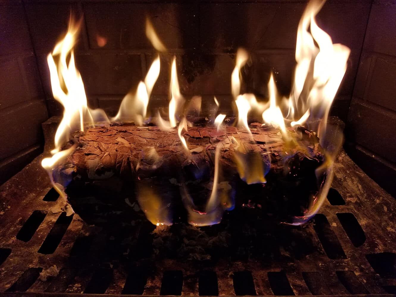 Firelog burning in a fireplace, flames are bright yellow and orange.