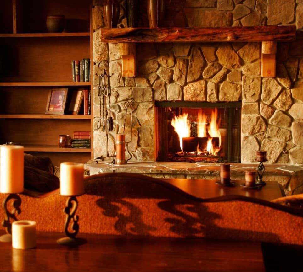 Fireplace with burning fire, stone surround, wood mantle, bookshelves, candles.