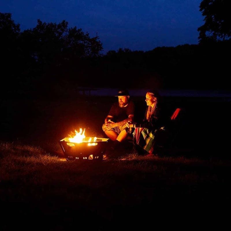 Two people sit by a glowing fire pit at night, silhouetted against the dark landscape.