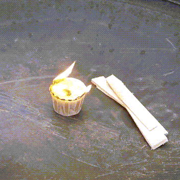 A burning Envirolog wax cup firestarter with kindling papers, set on a dark, textured surface