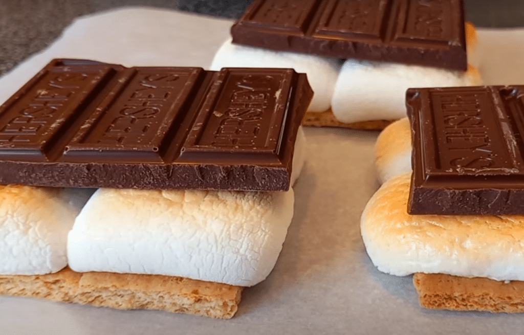 S'mores on parchment paper, with graham crackers, toasted marshmallows, and chocolate bars.