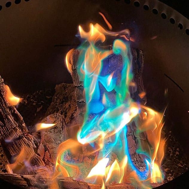 Fire burning with blue, green, and orange flames in a dark metal fire pit.