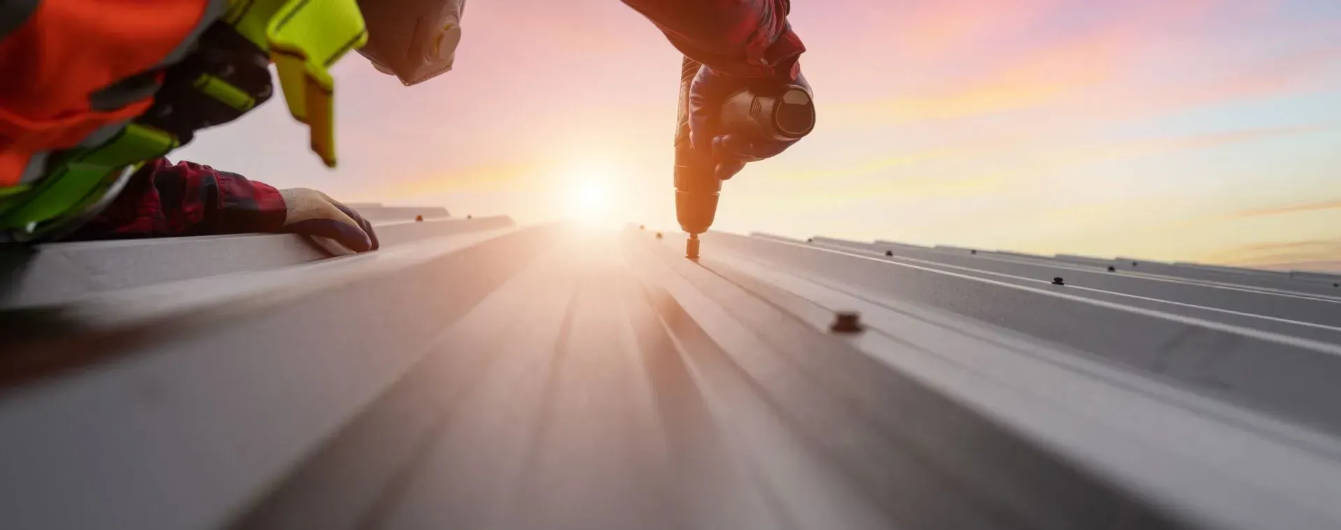 A construction worker is working on a roof at sunset.
