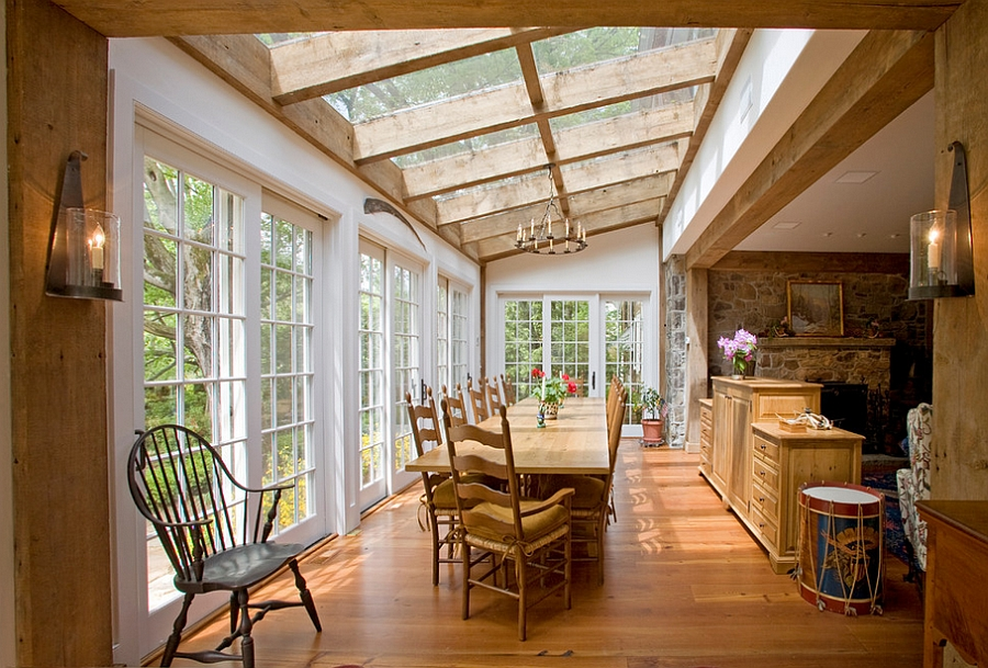Dining room with wood table and chairs, glass roof, windows, and sconces.