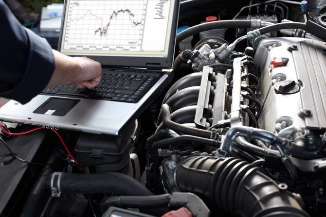 Mechanic using a laptop to diagnose a car engine in an open engine bay