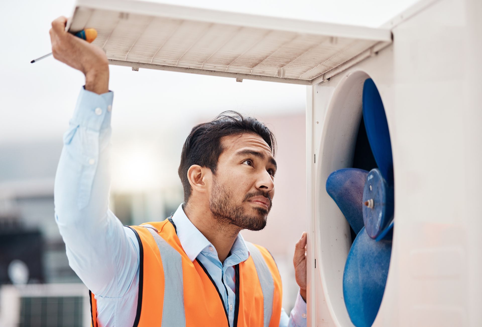A man in an orange vest is fixing a fan with a screwdriver.