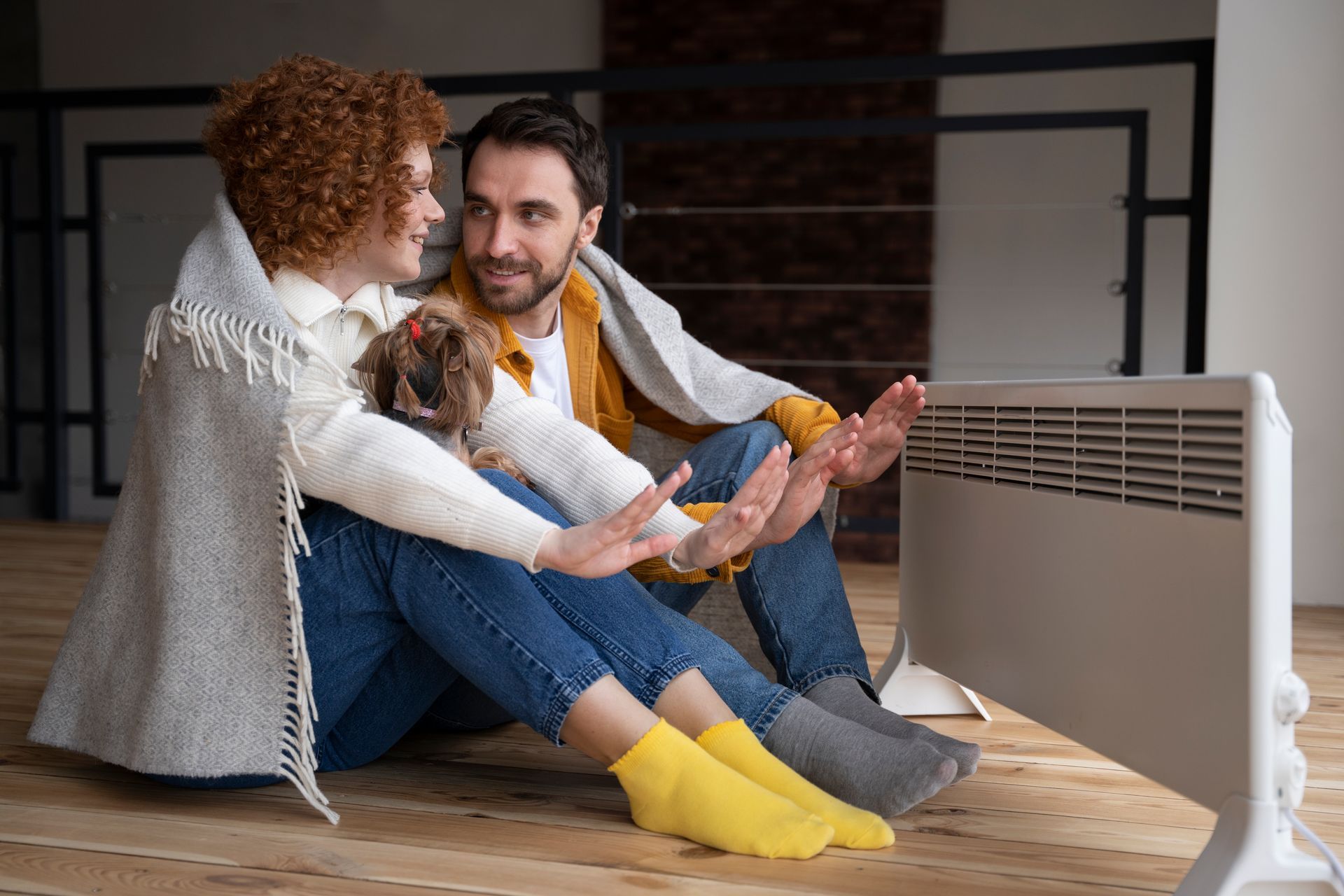 A man and a woman are sitting on the floor next to a heater.
