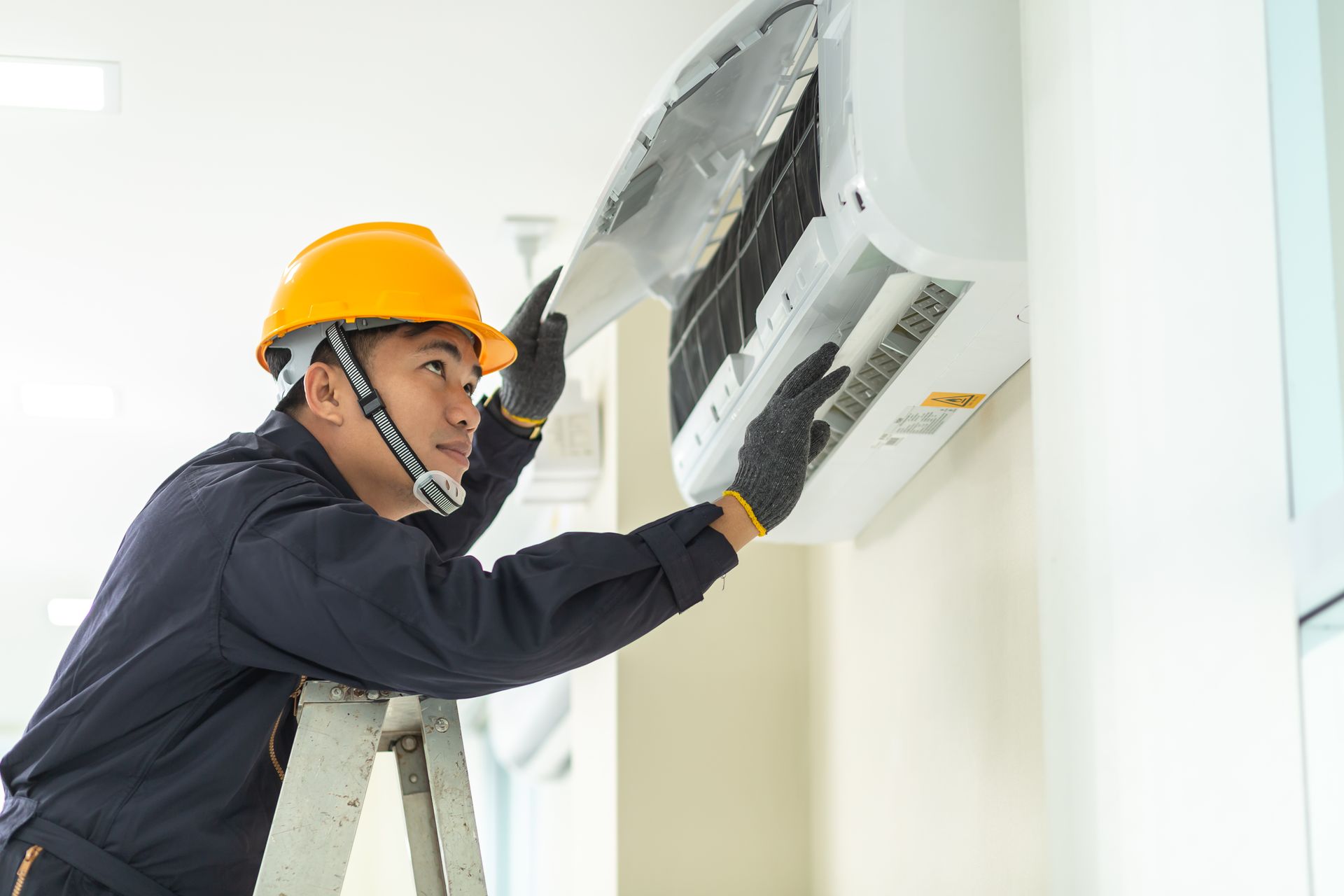A man is working on an air conditioner on a ladder.