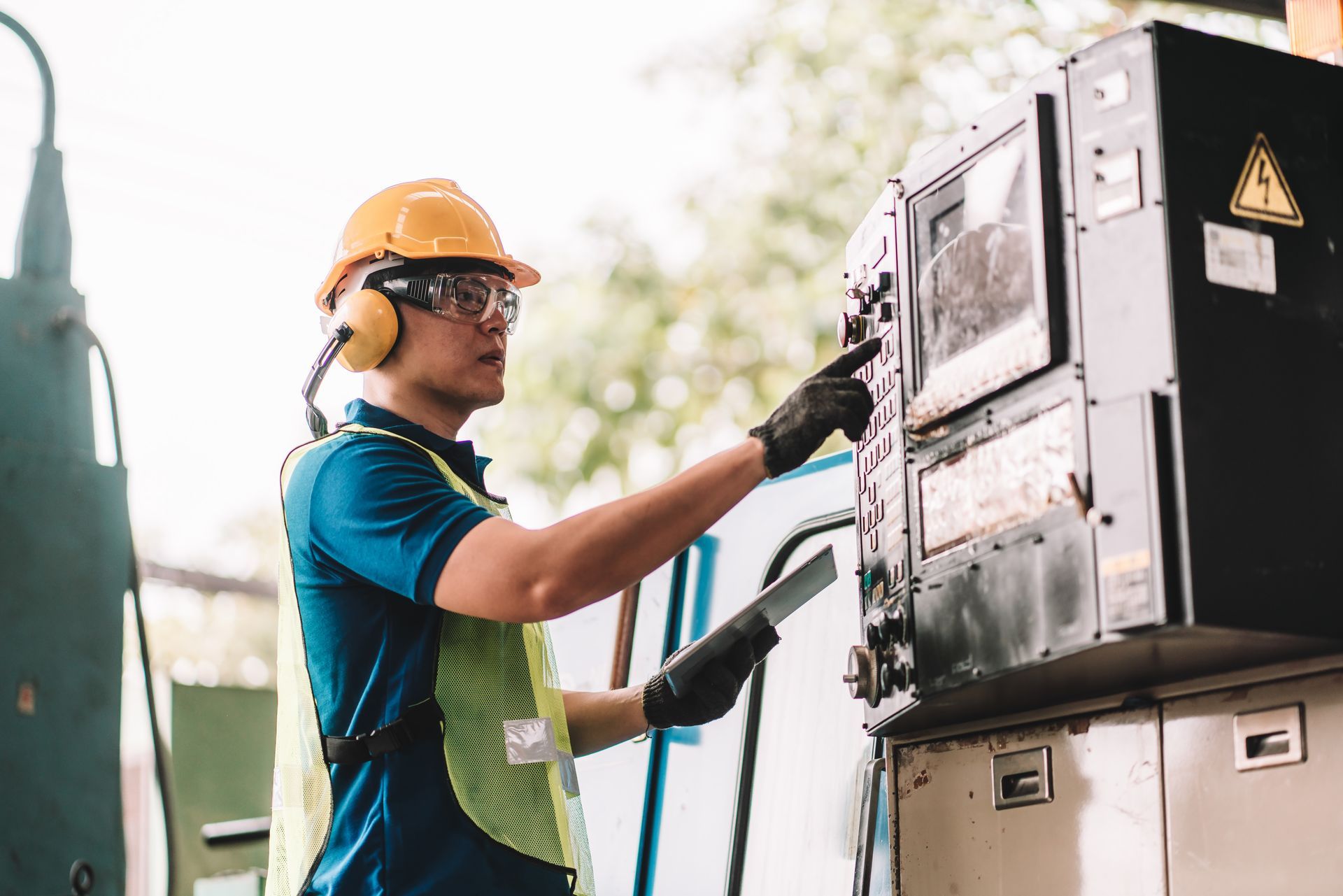 A man wearing a hard hat and ear muffs is working on a machine.