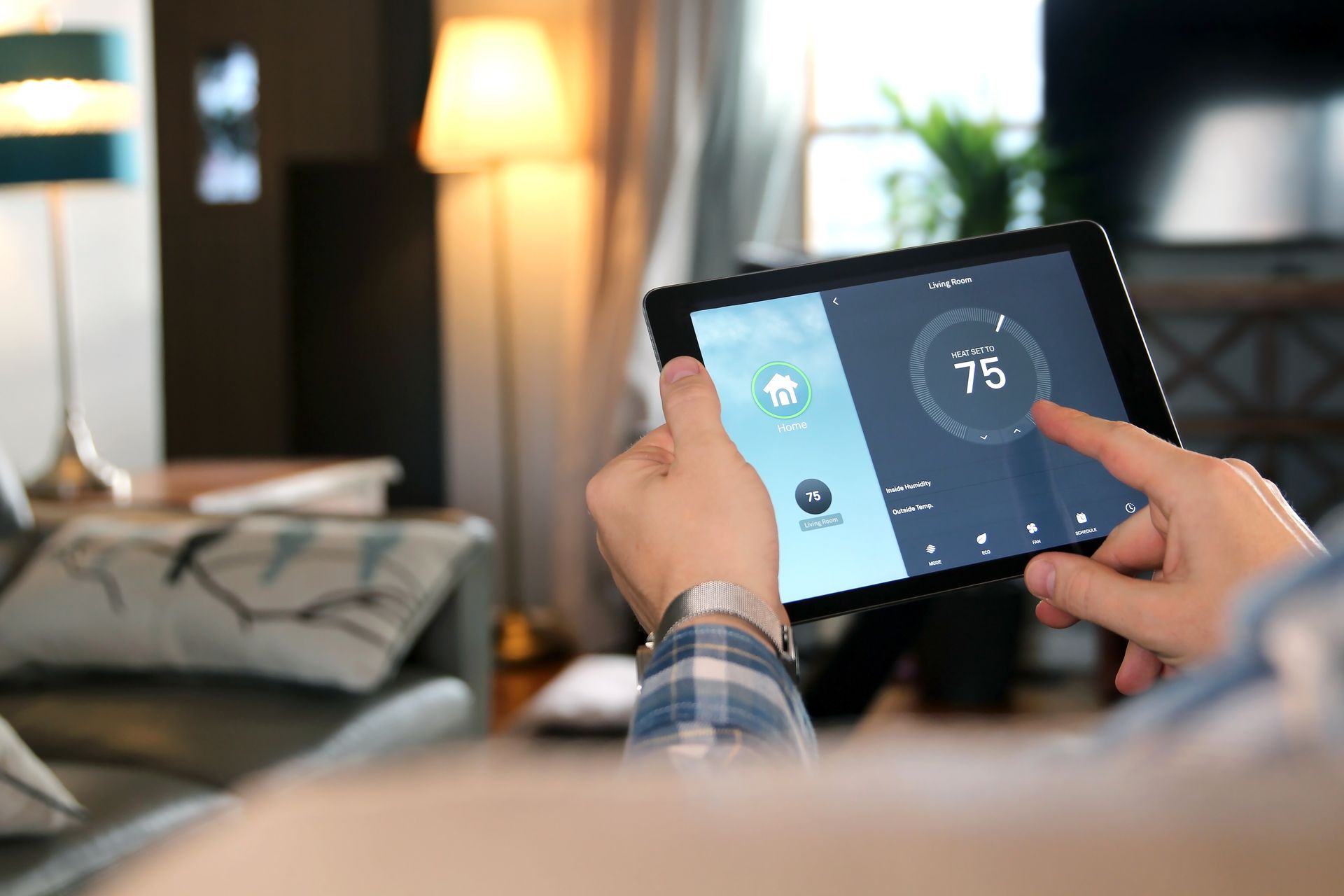 A person is holding a tablet with a thermostat on it.