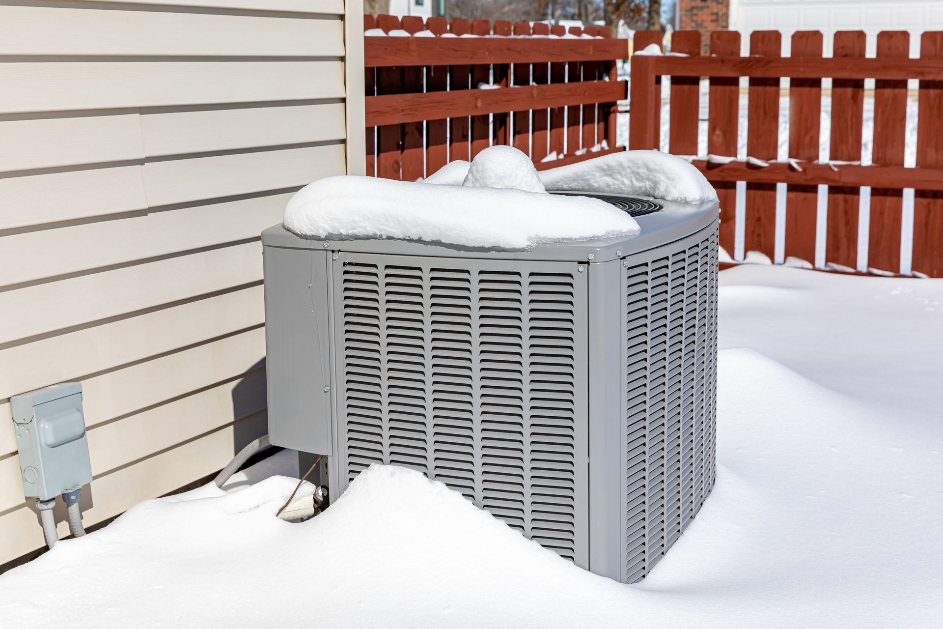 An air conditioner is covered in snow on the side of a house.