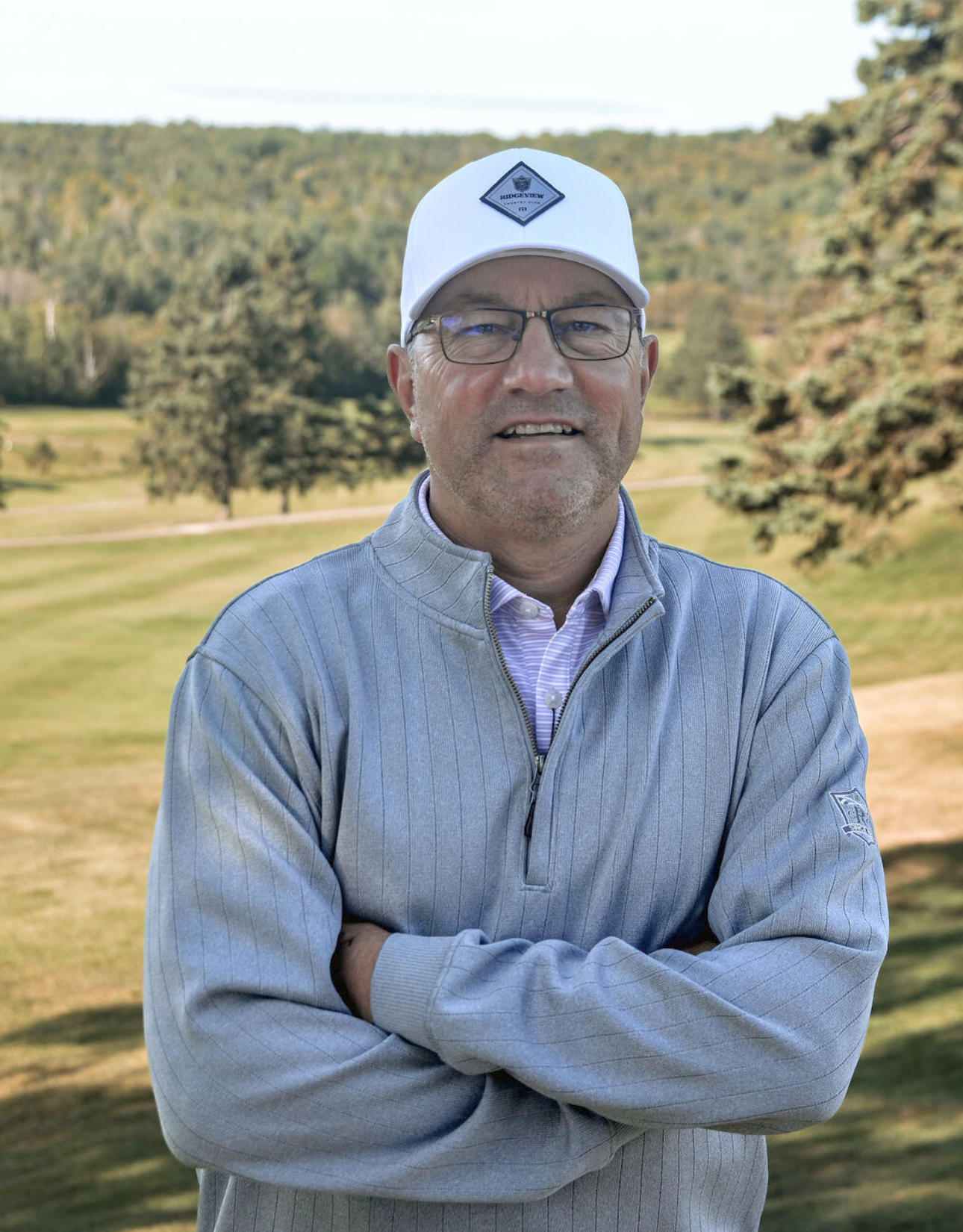 A man wearing a blue sweater and a white hat is standing in front of a tree.