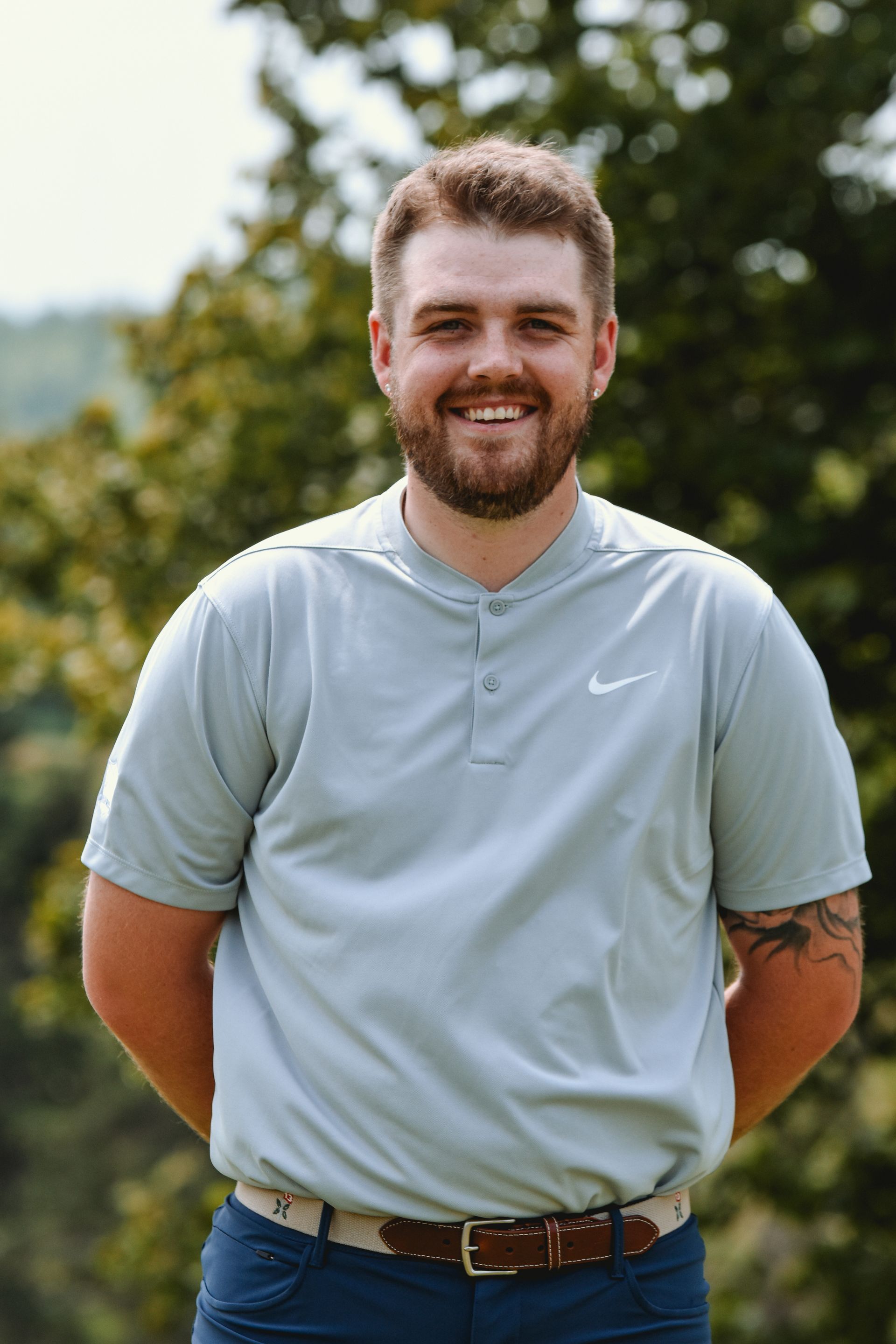 A man with a beard is wearing a nike shirt and smiling for the camera.