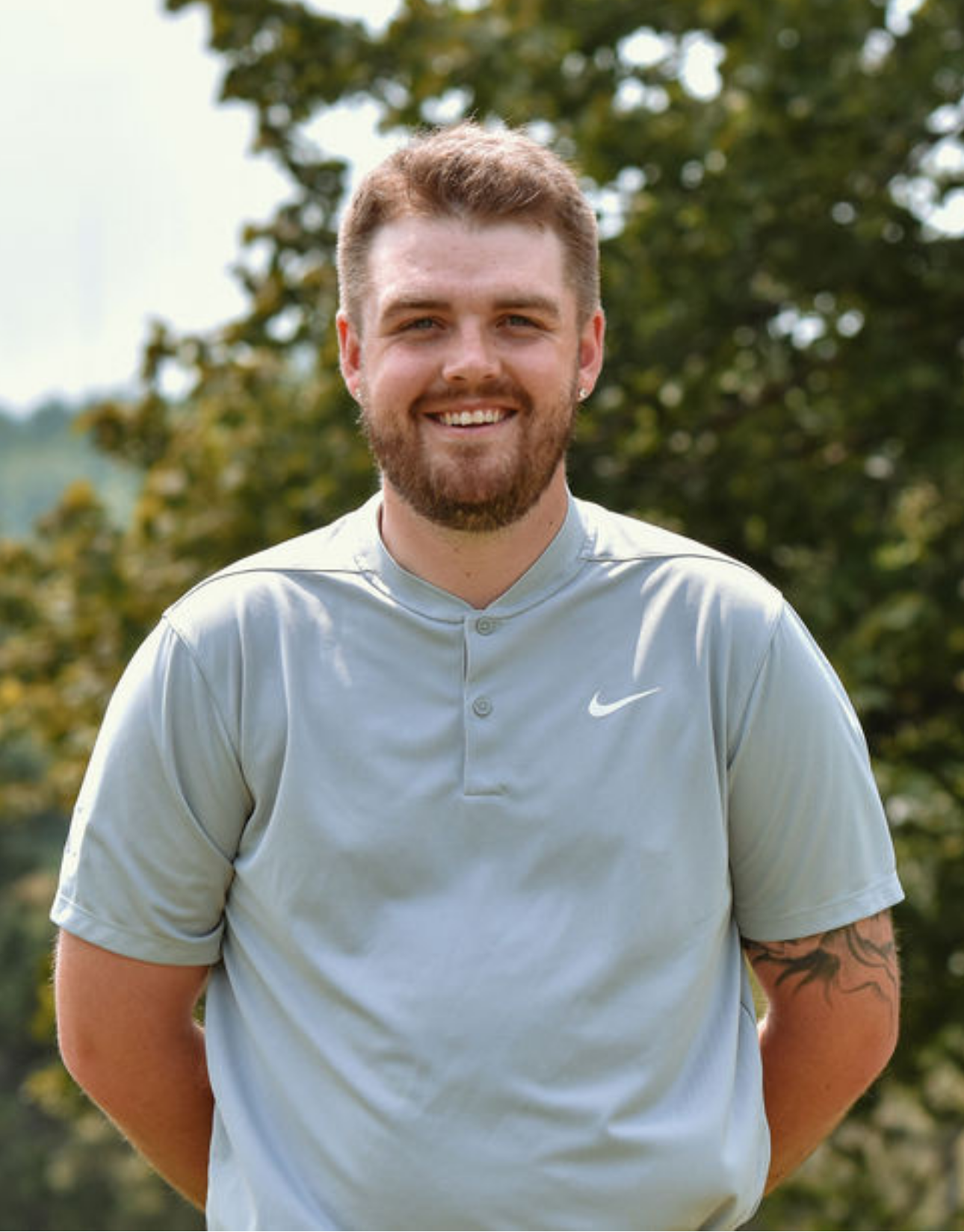A man with a beard is wearing a nike shirt and smiling for the camera.
