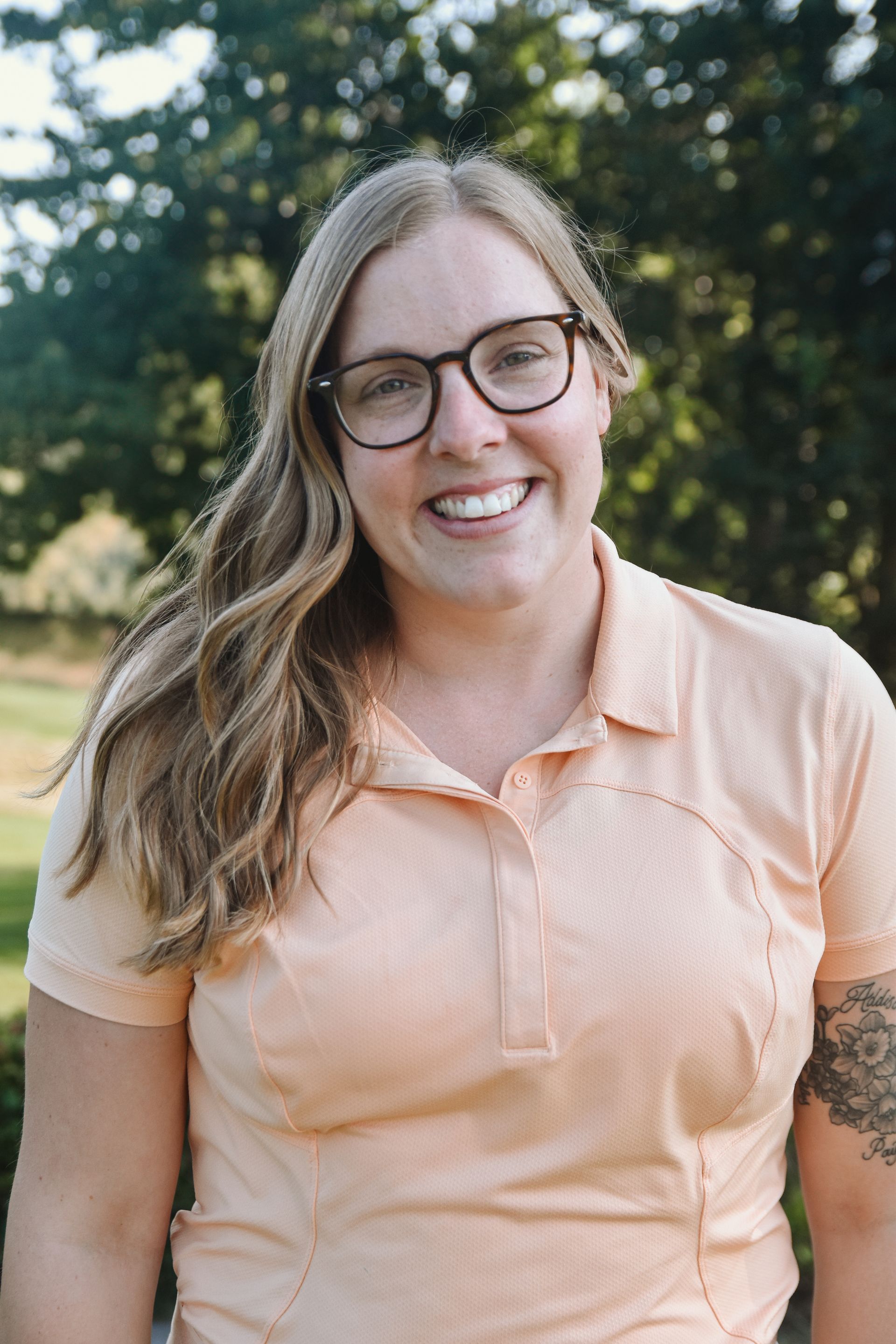 A woman wearing glasses and a polo shirt is smiling for the camera.