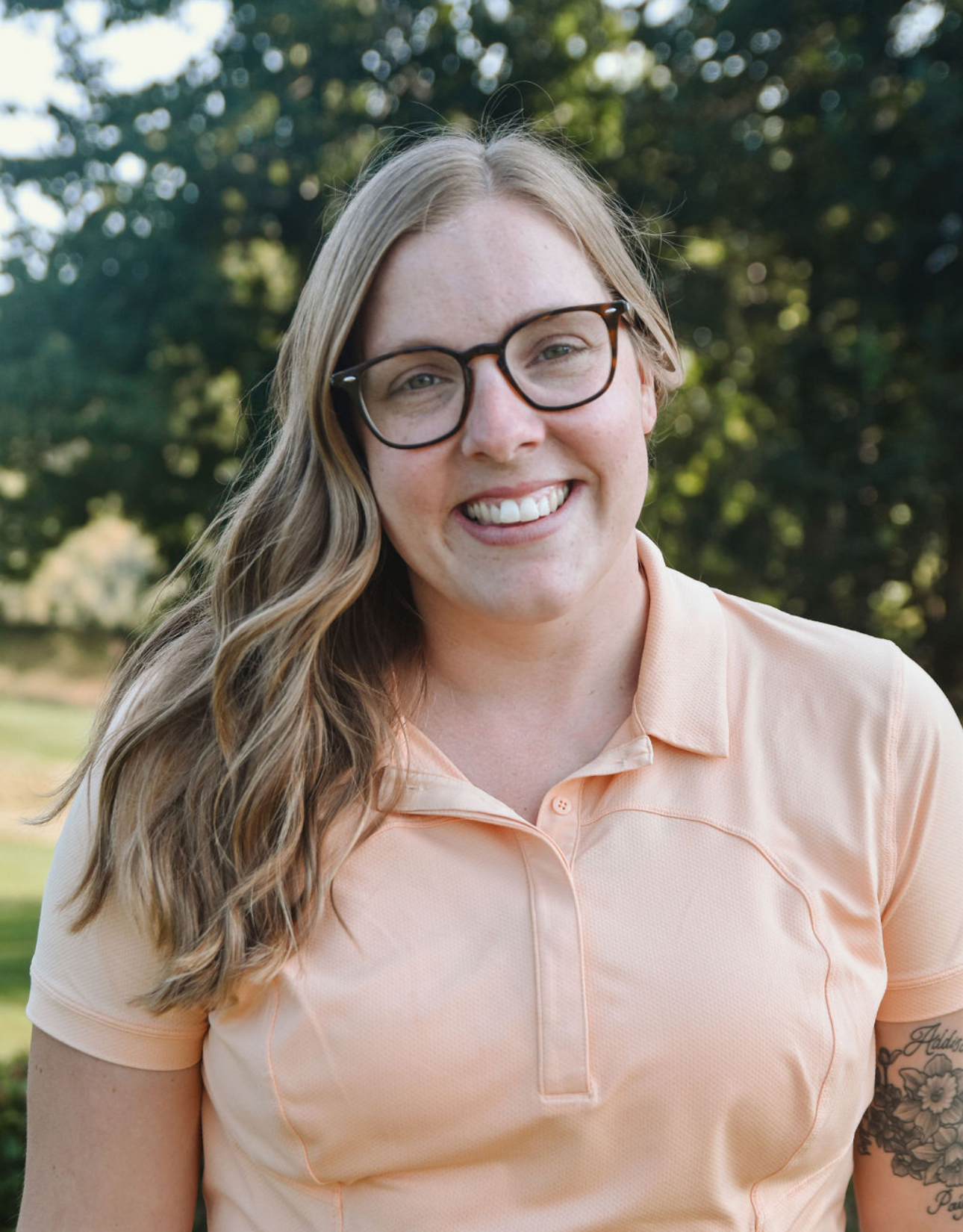 A woman wearing glasses and a polo shirt is smiling for the camera.