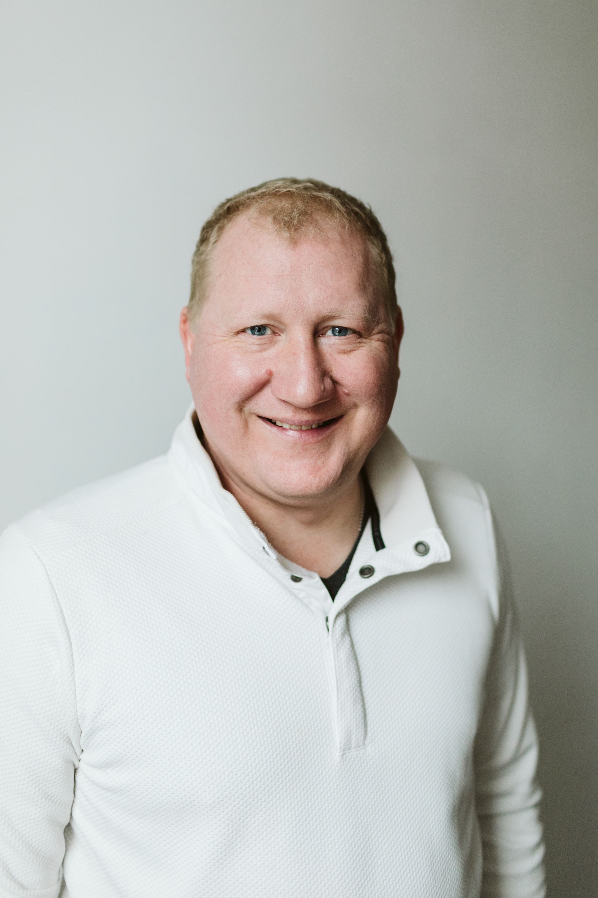 A man in a white sweater is smiling for the camera.