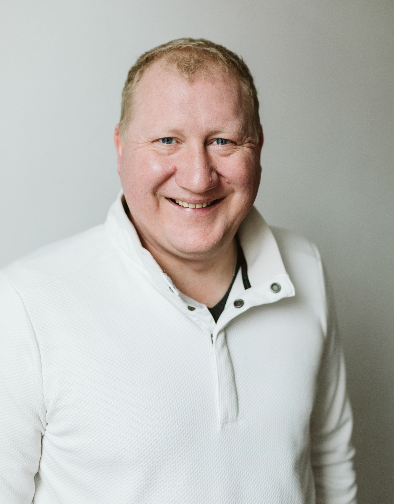 A man in a white sweater is smiling for the camera.