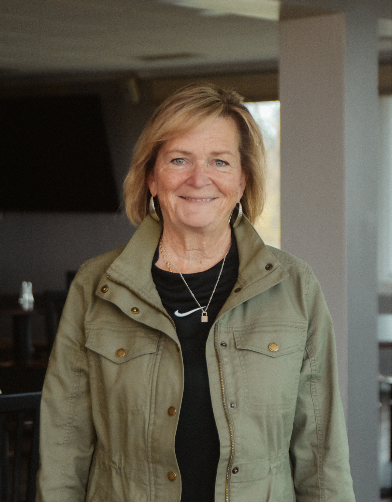 A woman wearing a green jacket and a black shirt is standing in a room.