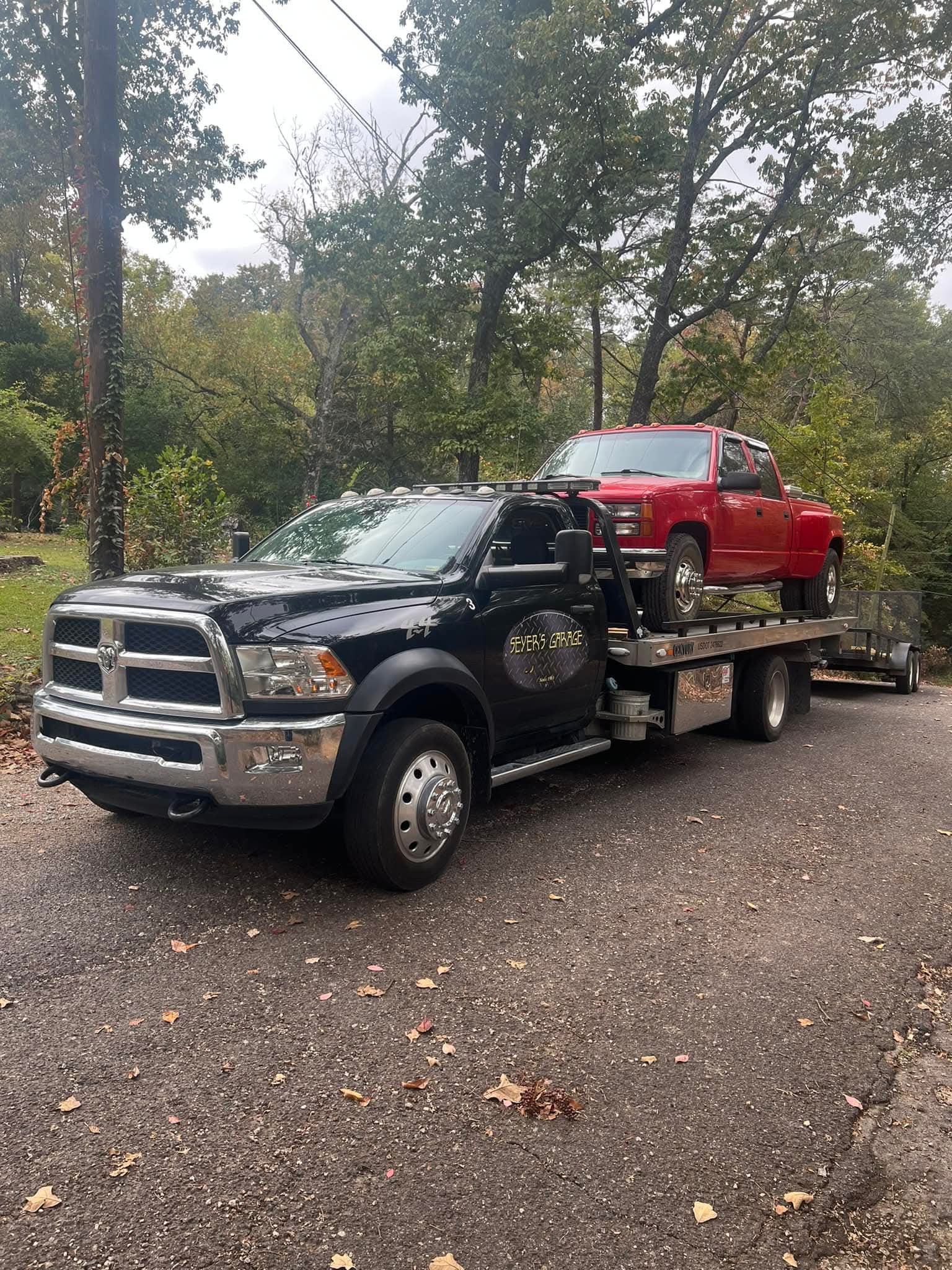 A black tow truck is towing a red truck on a trailer. | Seyer Garage