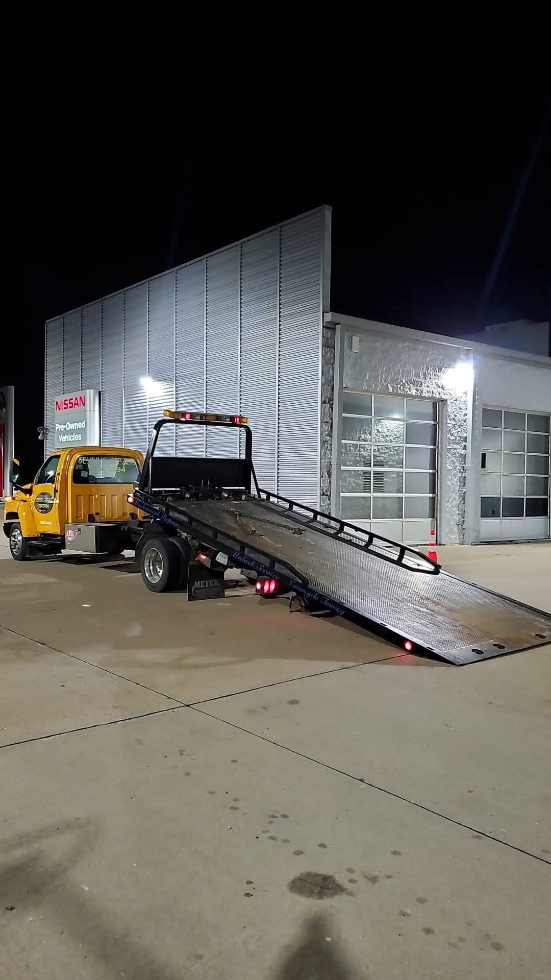 A yellow tow truck is parked in front of a building at night. | Seyer Garage