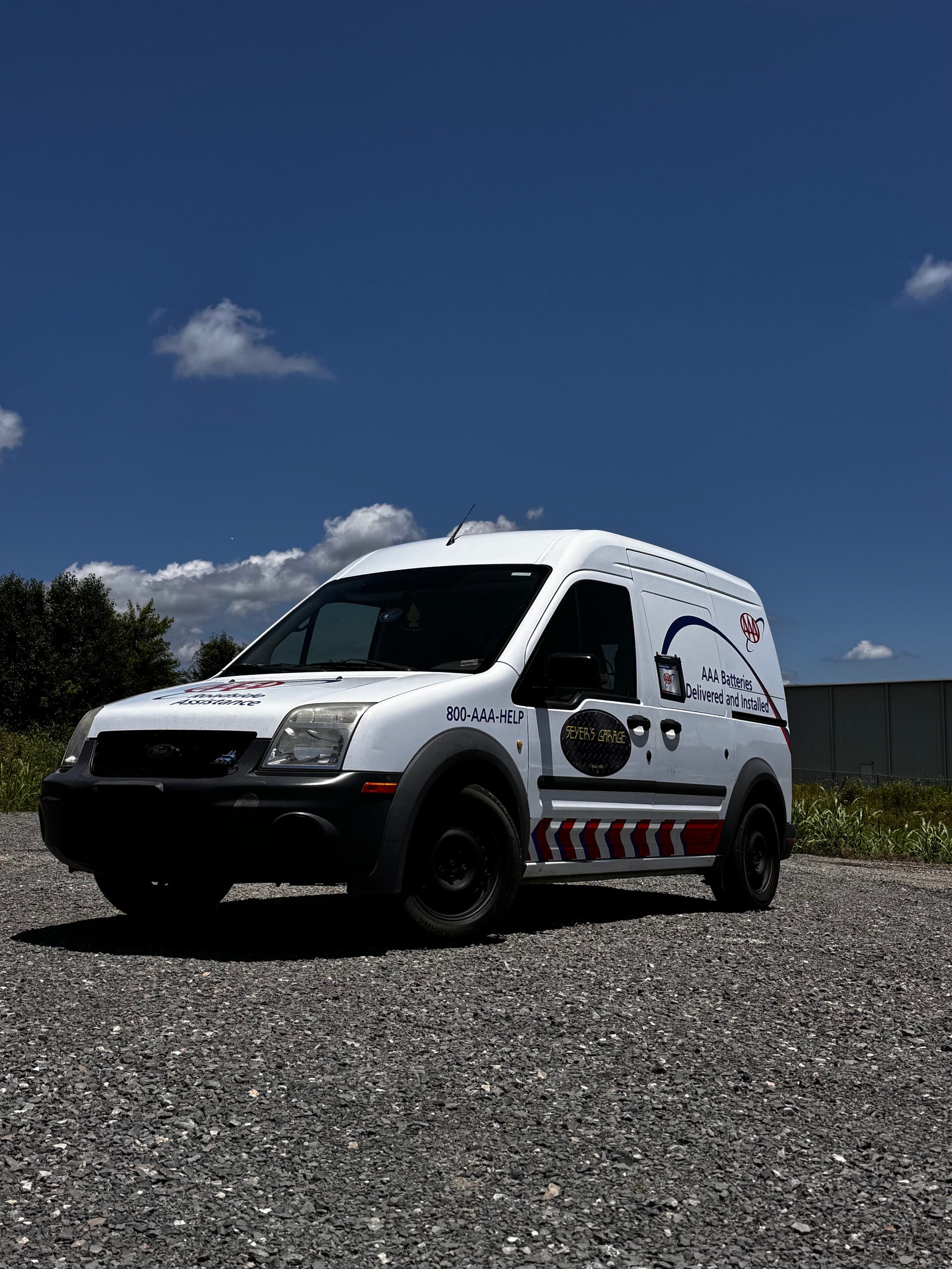 A white van is parked on a gravel road.