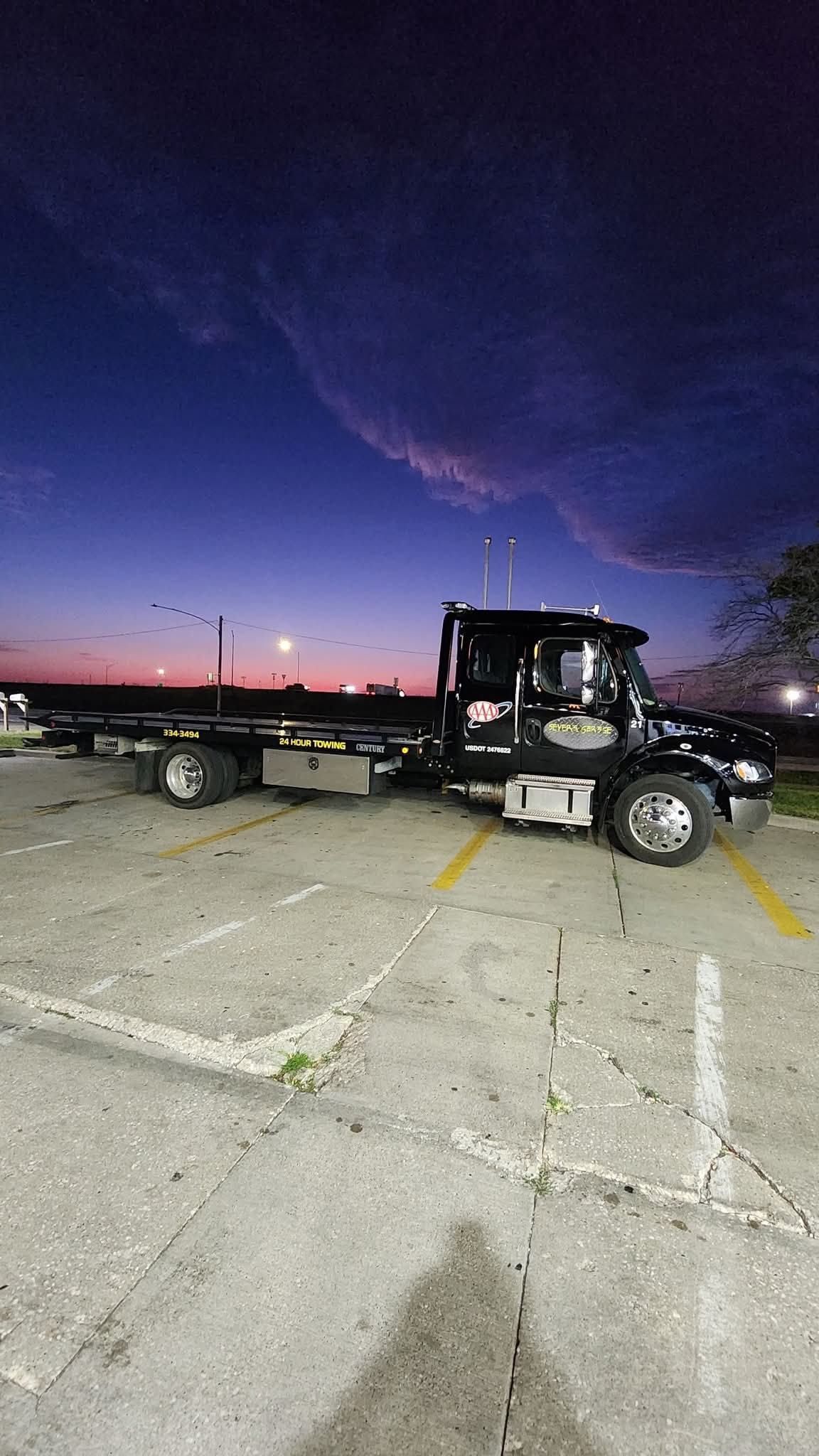 A tow truck is parked in a parking lot at sunset. | Seyer Garage
