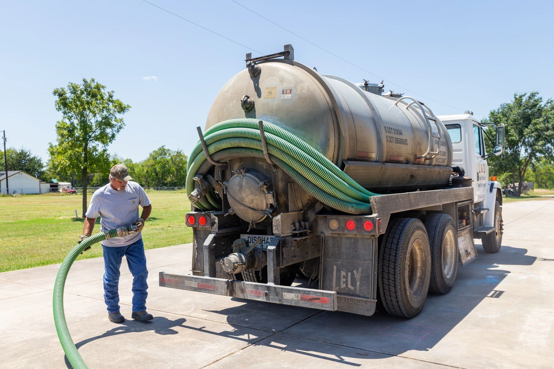 Man connecting hose to septic tank truck. Outdoors, bright day.