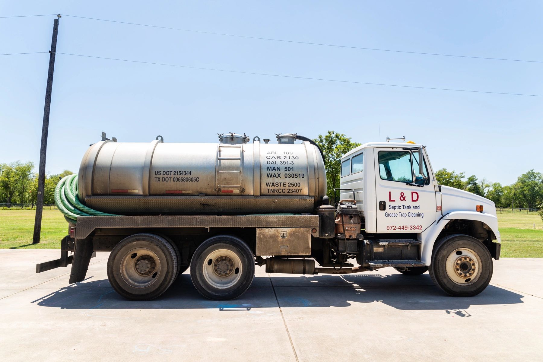 Septic truck on a sunny day with green hose, parked on concrete.