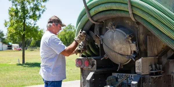 Man in gloves working on a septic tank truck, outdoors.